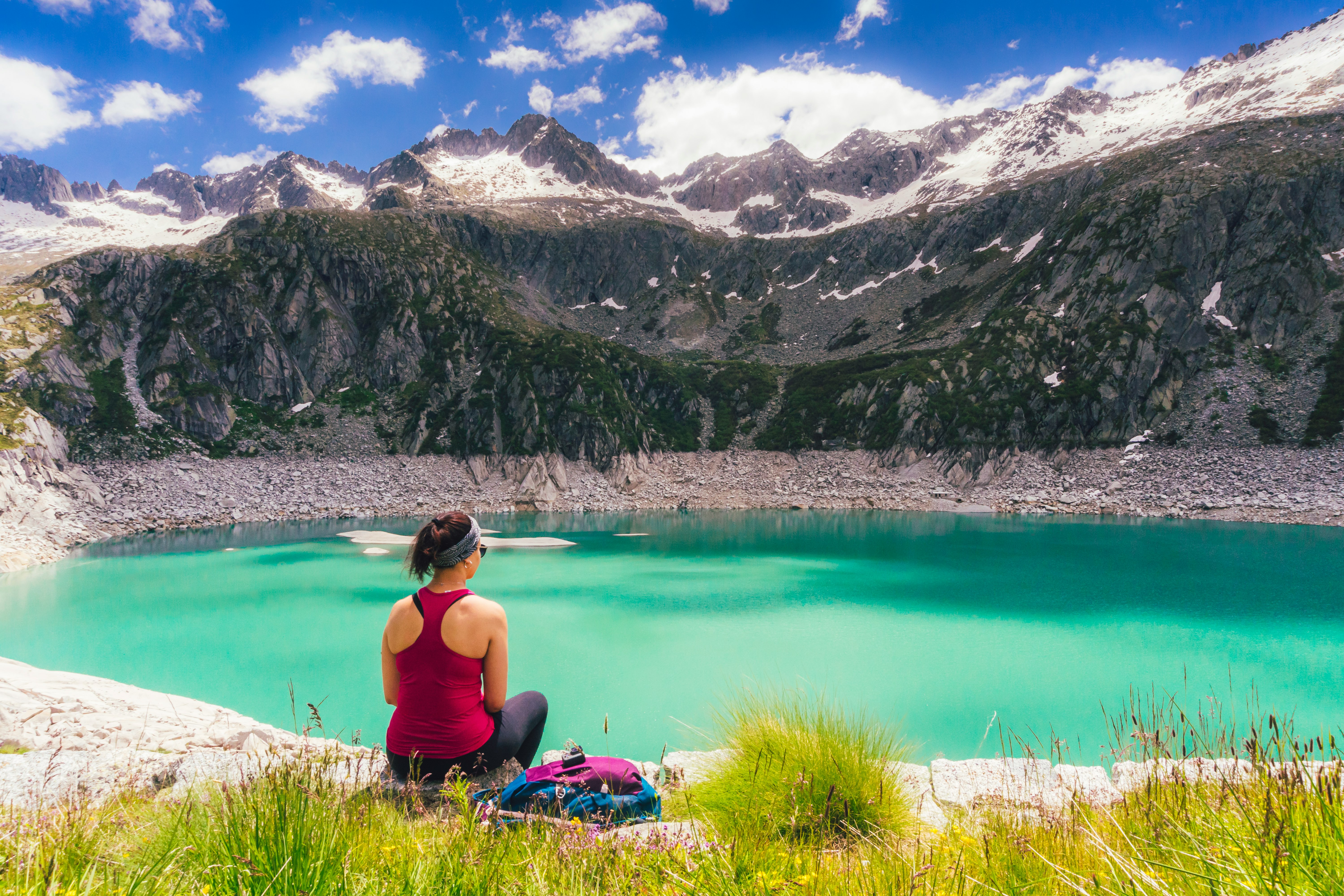 woman in black tank top sitting on green grass near lake during daytime